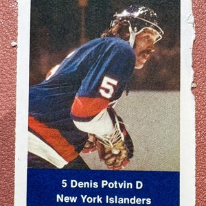 May include: A vintage hockey card featuring Denis Potvin of the New York Islanders. The card shows Potvin in his blue and orange jersey with the number 5. The card has a white border and a blue banner with the player's name and team.