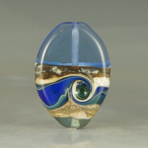 May include: An oval-shaped glass bead with a blue top and a swirling ocean design. The bead features shades of blue, brown, white, and green, with a hole running vertically through the center. The design evokes a seascape.