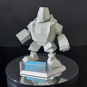 May include: A light gray, geometric figure of Barret Walace, a character from Final Fantasy VII, stands on a silver base. The figure has a blocky design with angular features and is displayed on a reflective surface. The name "Barret Walace" is printed on a blue label.