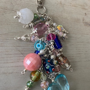 May include: A colorful charm keychain with a silver clasp and a variety of beads, including pink, blue, green, and white. The keychain features a heart-shaped charm, a clear glass bead, and a blue eye charm.
