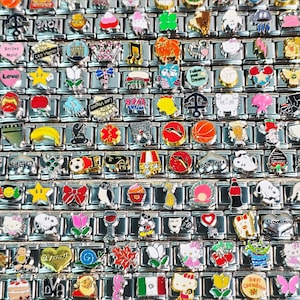 May include: A collection of colorful charm links with various designs, including hearts, stars, and travel-themed charms. The charms are made of metal and feature enamel details. Some charms have text like "Love" and "Las Vegas".