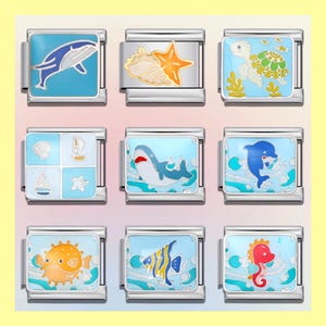 Op de afbeelding: Negen zilverkleurige bedelarmbanden met ontwerpen met oceaanthema. Elke bedel heeft een ander zeedier of element, waaronder een walvis, zeester, zeeschelp, schildpad, haai, dolfijn, kogelvis, tropische vis en zeepaardje, allemaal tegen een blauwe achtergrond.