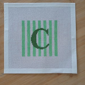 K&ouml;nnte beinhalten: Ein quadratisches Stickleinen mit wei&szlig;em Netzgewebe-Hintergrund und einer Reihe vertikaler hellgr&uuml;ner Streifen. Zentriert &uuml;ber den Streifen befindet sich ein dunkelgr&uuml;ner Buchstabe C, der in einer fetten Serifenschrift &uuml;ber das Streifenmuster gestickt ist.