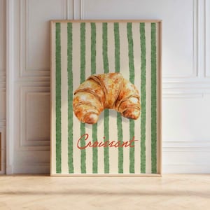 May include: A watercolor illustration of a croissant on a green and white striped background. The word "Croissant" is written in red cursive below the croissant.