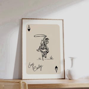 May include: A black and white illustration of a cowboy riding a horse and lassoing. The image is on a beige background with the text "Easy Cowboy" and the Ace of Spades card symbol.