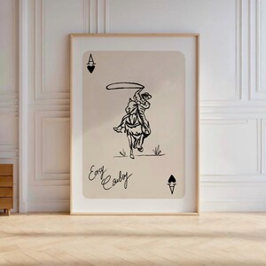 May include: A black and white illustration of a cowboy riding a horse and lassoing. The image is on a beige background with the text "Easy Cowboy" and the Ace of Spades card symbol.