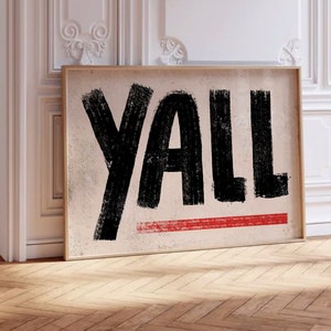 May include: A framed canvas print with the word "Y'ALL" written in large, black, brushstroke letters on a beige background. A thin red line is painted across the bottom of the canvas.