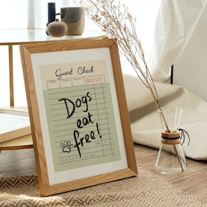 May include: A framed print with a wooden frame. The print is a guest check with the words "Dogs eat free!" written on it. The print also includes a paw print and the text "Thank You! Please Come Again."