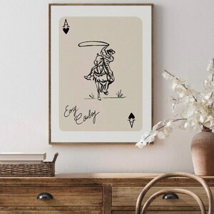 May include: A beige card with a black illustration of a cowboy riding a horse and lassoing. The card has the letter A and a spade symbol in the top left and bottom right corners. The text "Easy Cowboy" is written in cursive at the bottom of the card.
