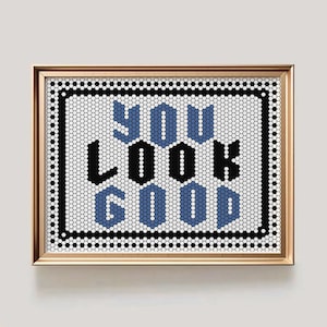 Puede incluir: Obra de arte enmarcada con la frase "YOU LOOK GOOD" en un diseño de mosaico. El texto es negro y azul sobre un fondo blanco, enmarcado en dorado.