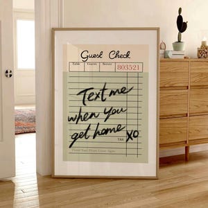 May include: A framed print featuring a stylized guest check design. The top section reads "Guest Check" with fields for table, guests, and server. The main text says "Text me when you get home XO". The print has a neutral color palette.
