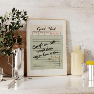 May include: A framed print of a vintage-style guest check with the text "Barista was cute, would have coffee here again" written in black cursive. The check has a green background and brown lines. There is a heart drawn next to the text and a coffee stain on the bottom right corner.