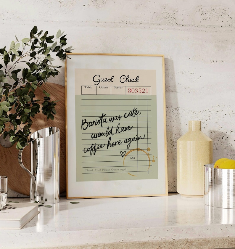 May include: A framed print of a vintage-style guest check with the text "Barista was cute, would have coffee here again" written in black cursive. The check has a green background and brown lines. There is a heart drawn next to the text and a coffee stain on the bottom right corner.