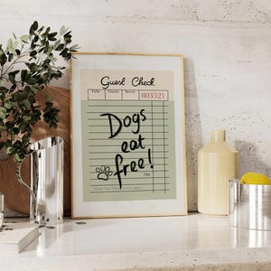 May include: A framed print resembling a guest check, with the words "Dogs eat free!" in black script. The print has a beige background with a paw print and the text "Thank You! Please Come Again."