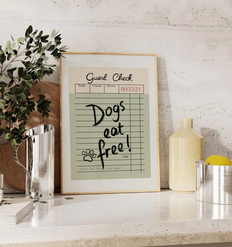 May include: A framed print resembling a guest check, with the words "Dogs eat free!" in black script. The print has a beige background with a paw print and the text "Thank You! Please Come Again."