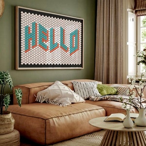 Könnte beinhalten: Ein braunes Ledersofa in L-Form mit weißen und schwarzen gemusterten Kissen, einem grünen Kissen und einer braunen Decke. An der Wand hinter dem Sofa hängt ein gerahmtes Mosaikbild mit dem Wort "HELLO" in blauen und orangen Buchstaben. Vor dem Sofa steht ein Holztisch mit einem Buch und zwei weißen Vasen.