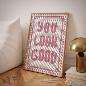 Może przedstawiać: Wydruk w ramie z mozaikowym wzorem w kolorze różowym i białym, na którym widnieje napis "You Look Good". Wydruk opiera się o białą sofę i złotą lampę.