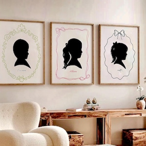Puede incluir: Tres retratos de siluetas enmarcadas de niños. Cada silueta negra está sobre un fondo blanco y enmarcada en un borde decorativo diferente. Los nombres "Daiana" y "Alliana" están escritos debajo. Los marcos se exhiben en una pared.