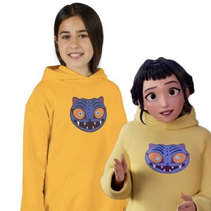 May include: Two yellow hoodies with a blue cat graphic. The cat has orange eyes and a white-toothed grin. The hoodies have a front pocket and a hood. One is worn by a person, the other by an animated character.