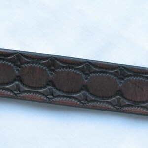 May include: A brown leather bracelet with a decorative embossed pattern and silver metal snaps.