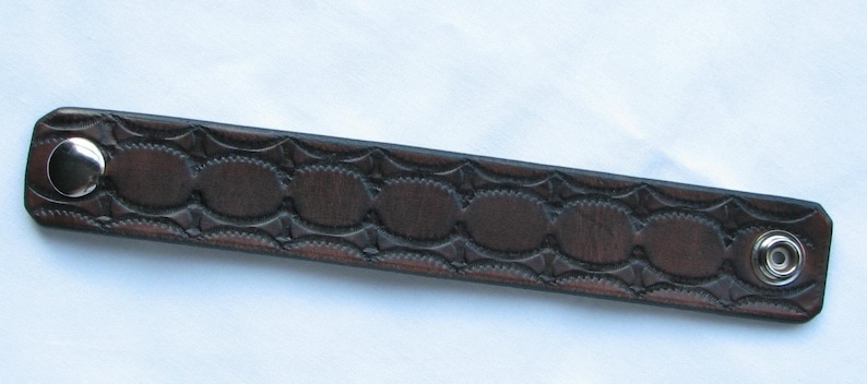May include: A brown leather bracelet with a decorative embossed pattern and silver metal snaps.