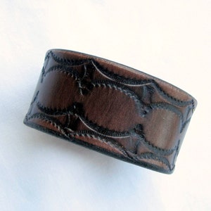 May include: A brown leather cuff bracelet with a decorative embossed pattern.
