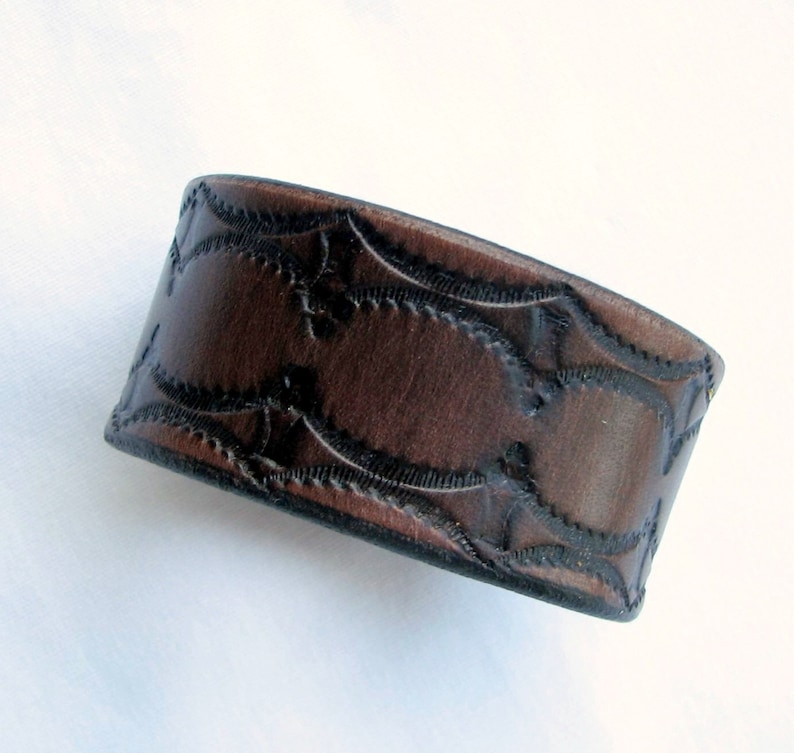 May include: A brown leather cuff bracelet with a decorative embossed pattern.