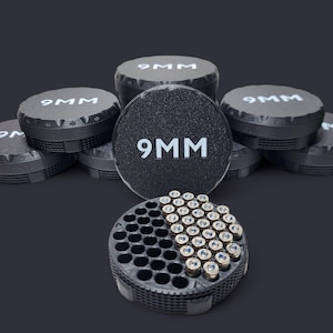 May include: A collection of black 9MM ammunition storage containers and a tray filled with bullets. The containers have textured sides and the text "9MM" in white. The tray holds multiple bullets.