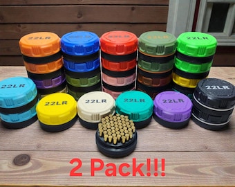 Peut inclure: Une collection de boîtes de rangement rondes et multicolores en plastique pour munitions 22LR, avec une prise texturée et l'inscription 22LR sur le couvercle. Un récipient ouvert au premier plan montre une grille de petites cartouches en laiton.