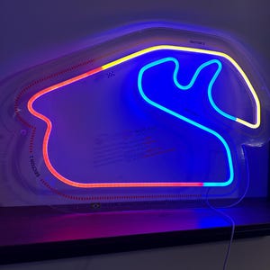 Peut inclure: Enseigne au néon en forme de circuit automobile, avec des lumières bleues, rouges et jaunes. L'enseigne porte les inscriptions "SECTOR 1" et "SECTOR 3". Le texte "INTERLAGOS AUTODROMO JOSE CARLOS PACE" est également visible.