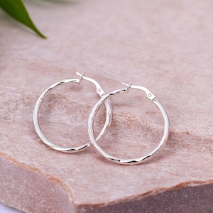 May include: A pair of silver hoop earrings with a twisted design. The earrings are made of metal and have a polished finish.
