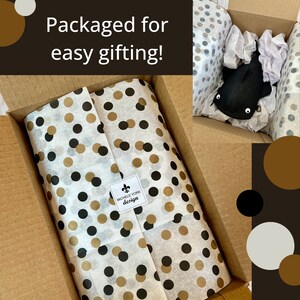 May include: A cardboard box with a wrapped gift and a plush toy. The gift is wrapped in white tissue paper with black and gold polka dots. The text "Packaged for easy gifting!" is visible.