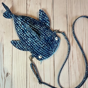May include: A blue and white patterned whale shark crossbody bag with a long adjustable strap. The bag has a cute whale shark face with white eyes.