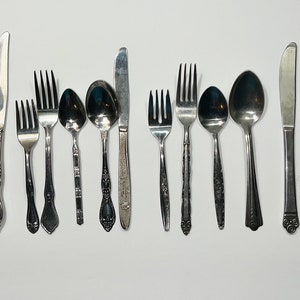May include: A set of 18 silver-toned cutlery pieces, including forks, spoons, and a knife. The cutlery is arranged in a row on a white surface.
