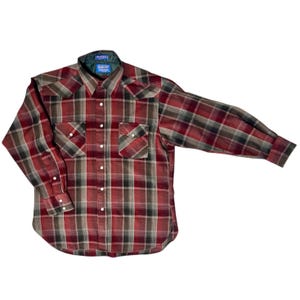 May include: A red, brown, and black plaid button-down shirt with two chest pockets and white buttons. The shirt has long sleeves and a collar with a green lining. The brand name is visible on the collar.