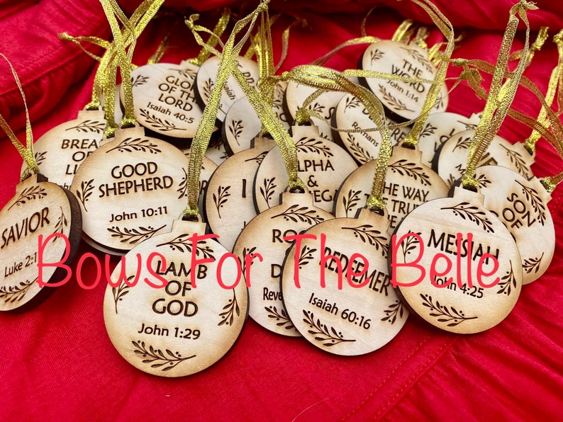 May include: A collection of wooden ornaments with religious text and scripture verses. The ornaments are round and have a rustic, wood-burned look. The ornaments are decorated with a simple leaf design. The text on the ornaments includes "Good Shepherd", "Lamb of God", "Savior", "Messiah", "The Word", and "Redeemer".