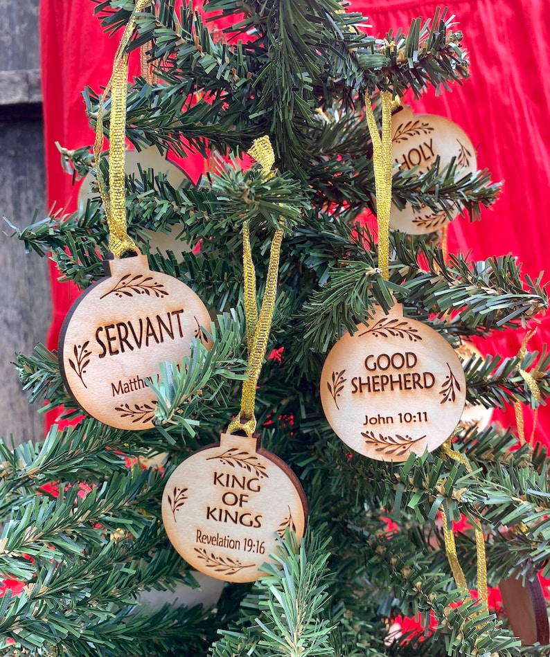May include: Wooden Christmas ornaments with religious themes. The ornaments are round and have a rustic brown color. The ornaments feature the words "Servant", "Good Shepherd", "King of Kings", and "Holy".
