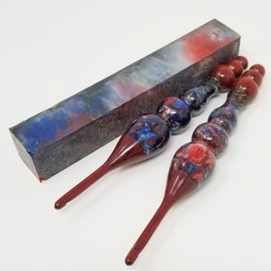 May include: Two red and blue crochet hooks with a swirl pattern and a red and blue, black and white marbled resin blank.