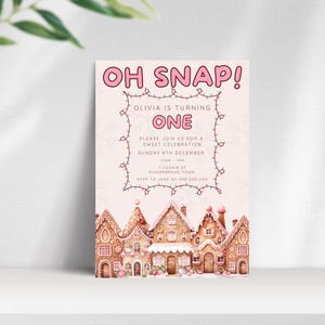 May include: Pink and white invitation with the text "OH SNAP!" and "Olivia is turning ONE". The invitation features a gingerbread house theme with illustrations of gingerbread houses and a string of pink lights.