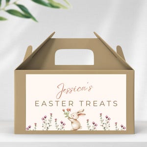 May include: A brown cardboard Easter treat box with a handle. The front features a cream-colored label with the text "Jessica's Easter Treats." A watercolor illustration of a bunny holding flowers is below the text.