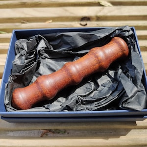 May include: A dark brown wooden rolling pin with a textured surface, resting in a blue box lined with black tissue paper.