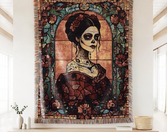 May include: A woven tapestry featuring a Day of the Dead woman with sugar skull makeup, surrounded by floral and stained glass-style elements. The color palette includes shades of brown, red, and teal. The tapestry has a fringed edge.