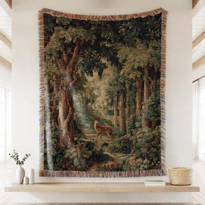 May include: A tapestry depicting a forest scene with a deer standing on a path. The artwork features lush green trees, a winding path, and a deer in the center. The tapestry has a fringed border and is displayed on a wall.