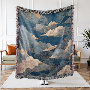 May include: A blue throw blanket with a cloud design. The blanket features a dark blue background with light blue, beige, and gold cloud patterns. The edges are finished with a fringe.