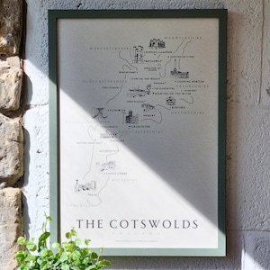 May include: A framed map of The Cotswolds, England, with a green frame. The map is in black and white, showing towns and landmarks in the region. The text "THE COTSWOLDS ENGLAND" is at the bottom of the map.