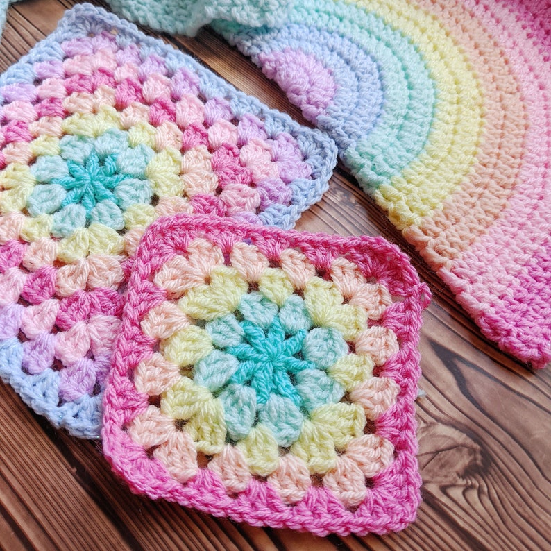 May include: Two colorful crocheted squares with a rainbow pattern. The squares are made with different shades of pink, blue, yellow, and green yarn.