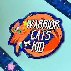 May include: A die-cut sticker featuring an orange cat with green eyes and a white star on its forehead. The sticker has a holographic finish and displays the text WARRIOR CATS KID in bold white letters next to a small white cat head icon.