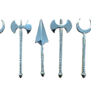 Puede incluir: Cinco armas en miniatura de color plateado, incluyendo una luna creciente, dos hachas y dos lanzas, se muestran sobre un fondo blanco.