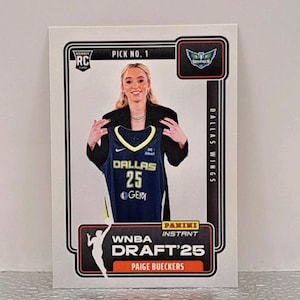 May include: A Panini Instant WNBA Draft'25 trading card featuring Paige Bueckers. The card shows Bueckers holding a Dallas Wings jersey with the number 25. The card has a white border with the Dallas Wings logo and "Pick No. 1" text.