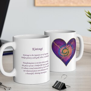 May include: White ceramic mug with a purple and gold heart design and the text "Kintsugi" and a definition of the Japanese art of repairing broken pottery with gold, silver, or platinum. The definition reads: "Transformation is not just about putting the pieces of one's broken life back together, it's about a total reinvention of self in which our shattered pieces are alchemized into a beautiful, thriving masterpiece."